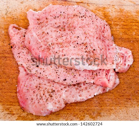Three cuts of pork tenderloin with spices on a wooden board ready to cook