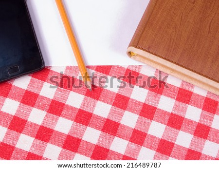 Notebook, white sheet of paper, pencil and smart-phone on a tablecloth