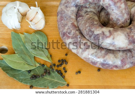 Uncooked homemade sausage on a wooden board with garlic, bay leaves and pepper