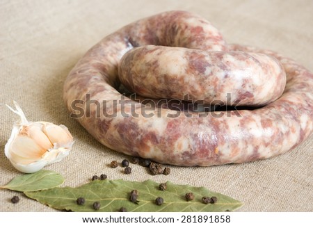 Uncooked homemade sausage on a gray sackcloth with garlic, bay leaves and pepper