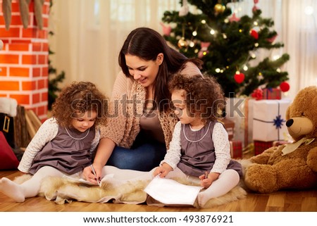 On Christmas Day my mother and two little twin daughters sitting on the floor in a room with a Christmas tree and decorations write a letter to Santa Claus in a happy new year.