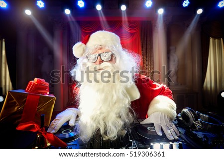 Dj Santa Claus at Christmas with glasses and snow mix on New Year\'s Eve event in the rays of light.