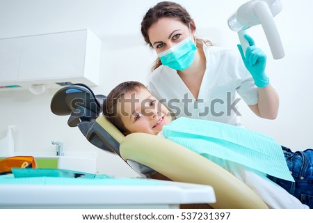 Beautiful kid boy smiling in dentist\'s chair the office treats teeth. Doctor mask and child looks at camera.