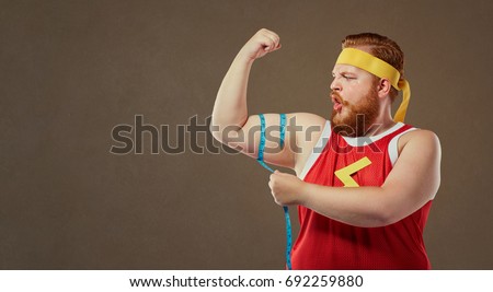 A funny fat man in sports clothes measures his arm with a centim