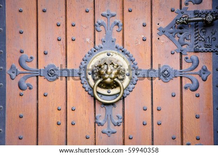 Lion head doorknocker on old-fashioned wooden door with metal elements