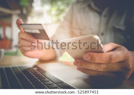Online payment, Man\'s hands holding a credit card and using smart phone for online shopping in coffee shop. vintage filter effect.