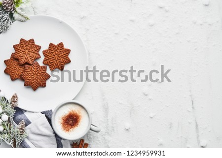 Gingerbread cookies with hot cocoa drink or eggnog on white marble table covered with snow. Top view of traditional Christmas gingerbread cookies with copy space.