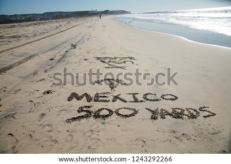 Words in sand. Mexico 500 yards with Arrow pointing towards Mexico written in the sand at the border between Mexico and the United States of America. Directional Signage.