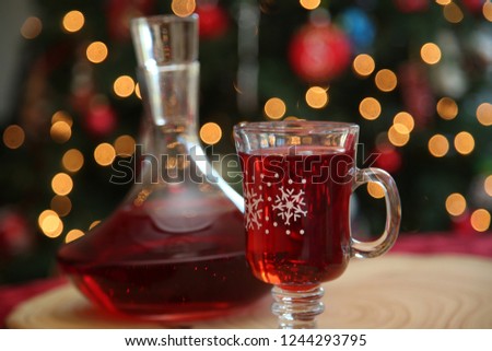 Christmas Wine. Wine or Juice in a Clear Glass Decanter and festive glass cup. Christmas Tree out of focus in background. Room for text Overlay. Christmas Images. Tree Trunk Cutting board on red.