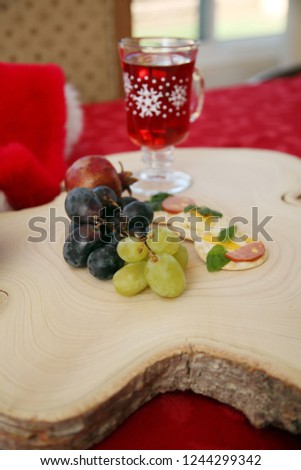 Wine, Cheese and Fruit Appetizers for Christmas. Appetizers consisting of cheeses, fruits, sausages, crackers and fresh herbs. Wooden Tree Stump Cutting board on a red table cloth.