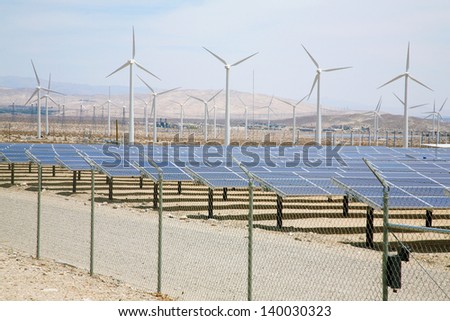 Solar Panels AKA- Photovoltaic Cells in a SOLAR FARM with Wind Turbines in the background collect and produce Electricity from Natural Renewable Resources of the Sun and Wind producing GREEN ENERGY