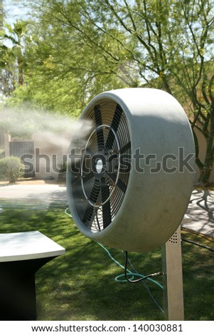 a water mister fan blows cool water into the air to cool down the area outside on a hot summer day