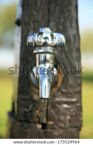 A stainless steel water tap drips water from its faucet during a drought in California outside. Shot with a Shallow Depth of Focus for a unique view of California\'s drought