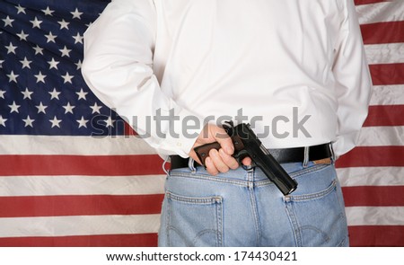 A under cover police officer or concerned citizen has a .45 caliber Pistol Concealed in his back waistband as he stands in front of the American Flag. The perfect image for your 2nd amendment rights