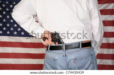 A under cover police officer or concerned citizen has a .45 caliber Pistol Concealed in his back waistband as he stands in front of the American Flag. The perfect image for your 2nd amendment rights