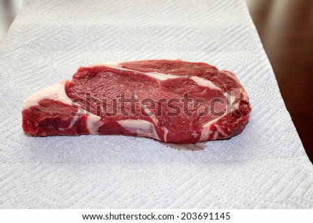 A Genuine Fresh Cut Steak lays upon a paper towel in preparation to be seasoned with salt and pepper and gently placed upon a hot BBQ grill to be Grilled to perfection for dinner.