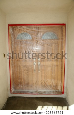 Home Front Doors are covered in plastic and held with painters tape in preparation for house painting of the stucco walls. Plastic sheeting is an important step in paint preparation.