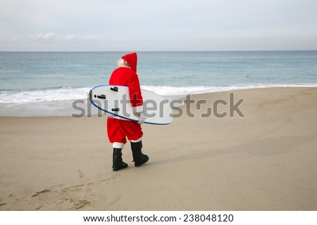 Surfing Santa Claus. Santa Claus holds his Blue Surfboard under his arm as he checks out the Waves at one of his Favorite Secret Surfing Spots. Santa loves Sports and Surfing. They call him Mr. Claus