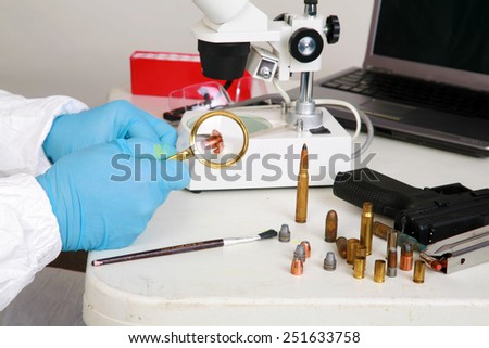 forensic analysis - a forensics lab technician examines a bullet and hand gun for finger prints, blood splatter, and any other residue or evidence to be used in a court case