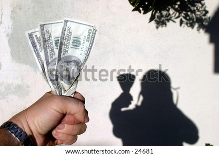 a hand holding two hundred and twenty dollars and the shadow of the holder in the background against a white stucco wall