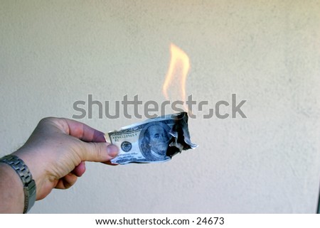 A hand holding a one hundred dollar bill and a twenty dollar bill on fire