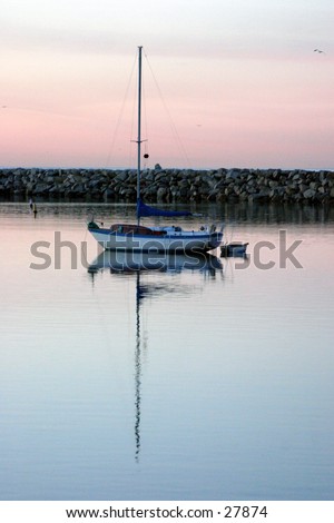 a lone sail boat sits in the water with its mirror reflection durring sunrise