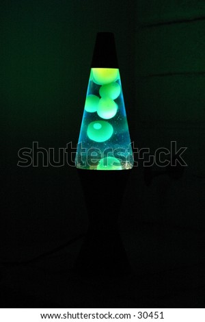 a lava lamp glows green with globes of lava float gently to the top and fall back down to the bottom of the container