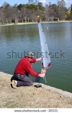 A man adjust and sets his remote controll sail boat in the water on a warm summer day