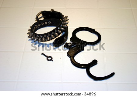 Black Spike collar and black hand cuffs with one hand cuff key on a white tile background.