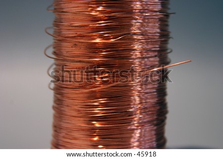copper wire rolled up on a spool sits on a gray background with great shadows and keylighting