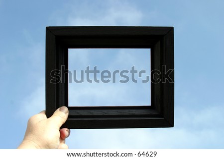 a black picture frame is held against a blue sky by a real human hand