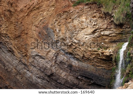layers of earth on a sheer cliff wall with a waterfall showing the age of the earth