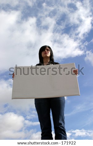 a young woman holds a blank white board against a blue sky with white fluffy clouds