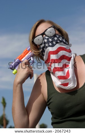 an insane young woman wearing a mask and hypnotic glasses woman points a squirt gun directly at her head