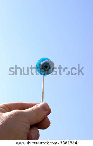 Eye Candy Series A blue lolly pop held against the blue sky with a Real Antique Glass Eye attached