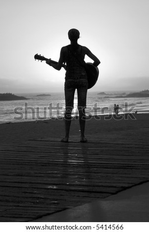 stock photo an unidentifiable young woman plays her guitar as the sun sets 
