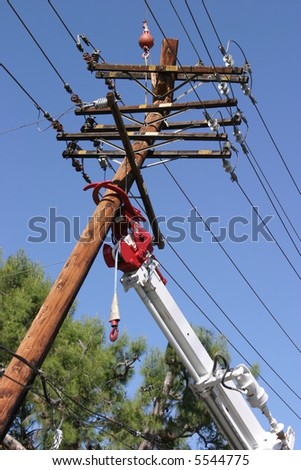 Workers with a crane with claws prepare to remove and replace a 95 foot utility pole broken by a car accident