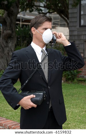 a business man wears a medical face mask or dust mask to protect himself and others from the flu and other airborn virusis while talking on his 1980s era car phone