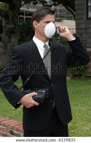 a business man wears a medical face mask or dust mask to protect himself and others from the flu and other airborn virusis while talking on his 1980s era car phone