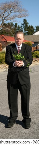 an enviromently friendly business man in a nice suit holds a green plant to save the earth from Global Warming