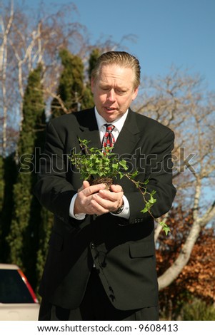an enviromently friendly business man in a nice suit holds a green plant to save the earth from Global Warming