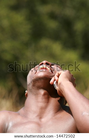 a handsome african american man laughs after recieving funny news on his cell phone