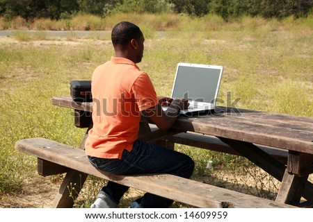 a man on a laptop computer outside in a park representing wireless connections and mobile business concepts