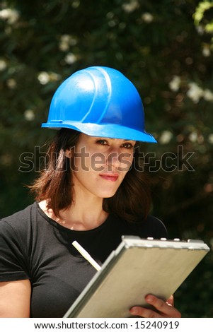 a beautiful young woman in a hard hat smiles and laughs at something she sees on a construction site