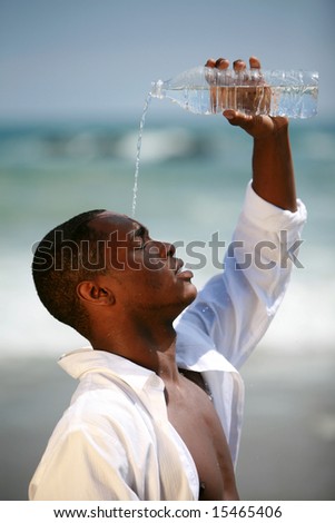 a handsome african american male model pours fresh cold water from a bottle on his head to cool down at the beach on a beautiful summer day