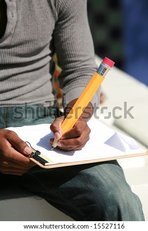 a young man takes notes on a sheet of paper with a giant pencil