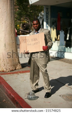 a thursty business man stands on a city street with a cardboard sign that reads 