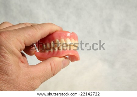 a human hand holds Genuine Dentures AKA False Teeth from a Dentist Office on grey