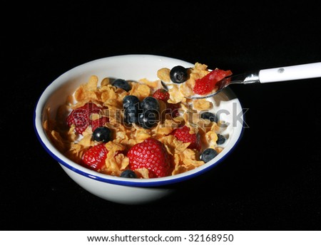 low key studio shot of spoon full of cereal in the foreground and a bowl of cereal with strawberries and blueberries in the background isolated on black