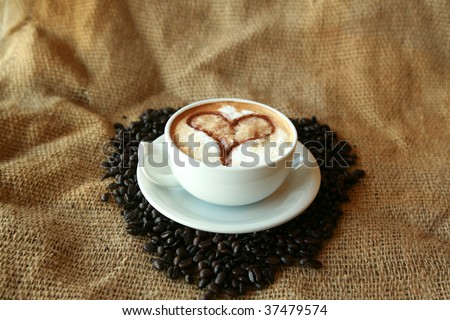 Coffee for Coffee Lovers, a cup of Coffee or  espresso with a Heart in the foam nestled in a bed of unground coffee beans on a burlap background